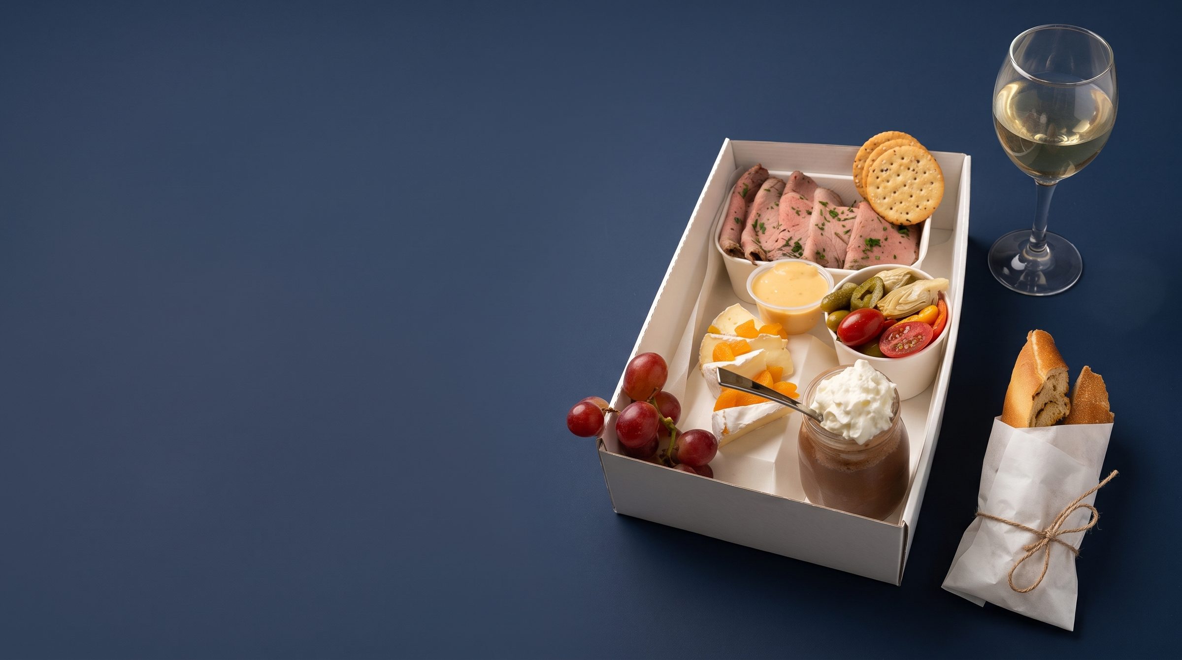 Boxed lunch with a sandwich, fresh salad and sides on a navy surface