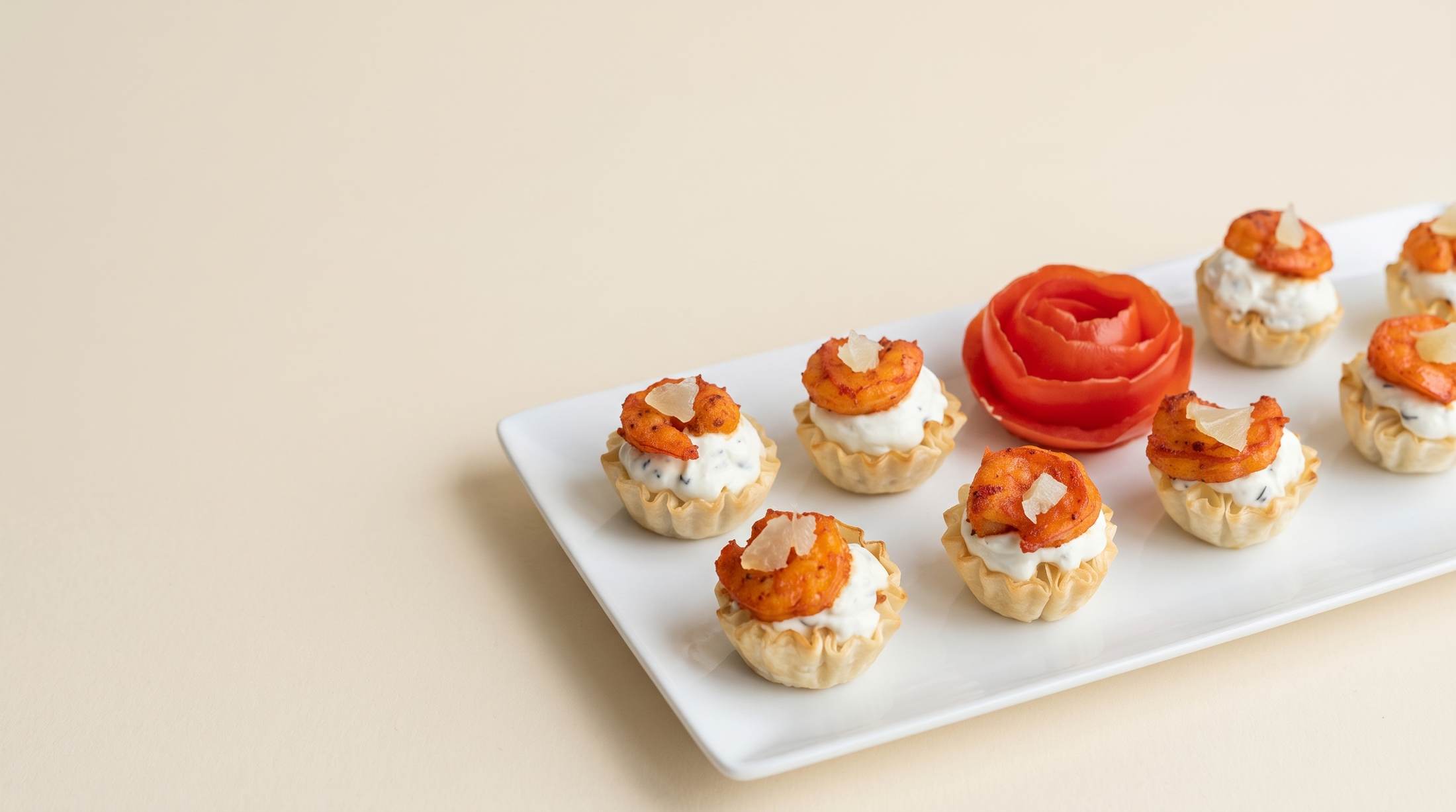Shrimp tartlets with a tomato rose garnish on a white serving platter