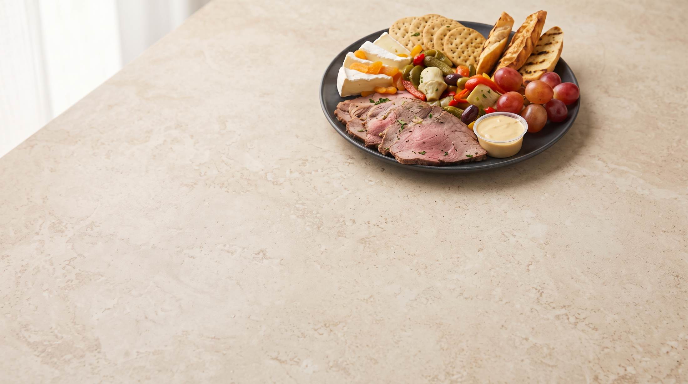 Roast beef charcuterie plate with cheeses, crackers, grilled bread, olives and grapes on a stone counter